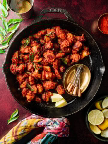 chicken 65 in a skillet with appetizer picks and garnishes